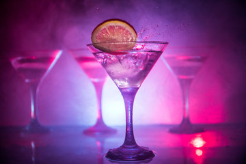 Martini cocktail glass in hand splashing on dark toned smoky background or colorful cocktail in glass with splashes and olives. Party club entertainment. Mixed light. Selective focus