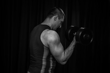 Obraz na płótnie Canvas athlete trains biceps hands with dumbbells in the center of workouts on a black background. training tools in the gym close-up