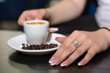 Girl hand with french nails polish manicure with espresso coffee cup on the desk in a bar on the saucer and blurred roasted coffee beans and cup. Close up, selective focus