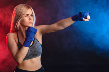 Young attractive kickboxing female fighter with blonde hair practicing punches. Kickboxer in blue...