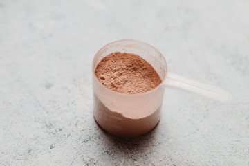 Scoop or spoon of whey protein with visible texture. Chocolate flavor. Concrete background