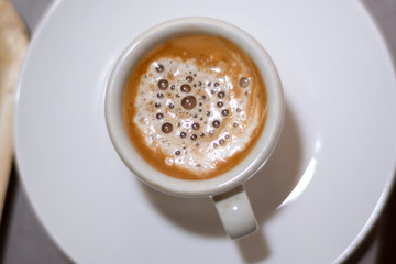 Top view of espresso coffee in a white cup on a saucer. Brown coffee with milk and bubble. Close up, selective focus