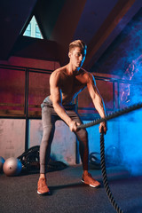 Caucasian bodybuilder practicing effective way to torch calories and enhance cardiovascular health. Full length photo. Battle rope training in a gym