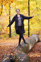 happy carefree young woman balancing on tree trunk in forest - enjoying active lifestyle in fall...