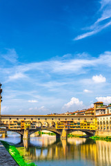 Ponte Vecchio stone bridge with colourful buildings houses over Arno River blue reflecting water in historical centre of Florence city, blue sky white clouds, vertical orientation, Tuscany, Italy