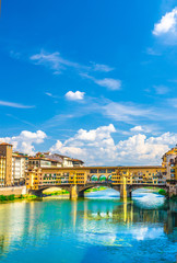 Fototapeta na wymiar Ponte Vecchio stone bridge with colourful buildings houses over Arno River blue reflecting water in historical centre of Florence city, blue sky white clouds, vertical orientation, Tuscany, Italy