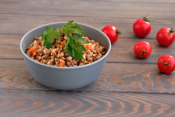 Buckwheat porridge with a sprig of parsley in a bowl and tomatoes on a dark rough wooden table. Rustic style. Traditional Russian dish.  Russian porridge