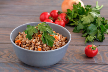 Buckwheat porridge with a sprig of parsley in a bowl and tomatoes on a dark rough wooden table. Rustic style. Traditional Russian dish.  Russian porridge
