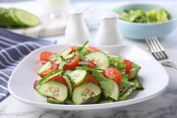 Plate of vegetarian salad with cucumber, tomato, lettuce and onion served on table, closeup