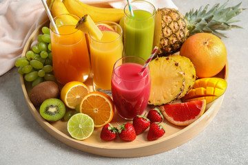 Wooden tray with glasses of different juices and fresh fruits on table