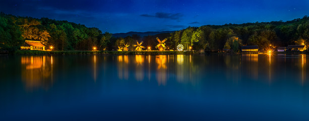 Landscape panorama with windmills at the blue hour in White Night of the Museums. Dumbrava lake, Astra Museum of Traditional Folk Civilization, Sibiu city, Romania