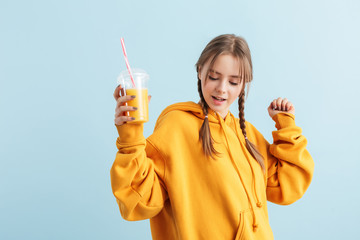 Young attractive girl with two braids in orange hoodie holding plastic cup with juice in hand while...