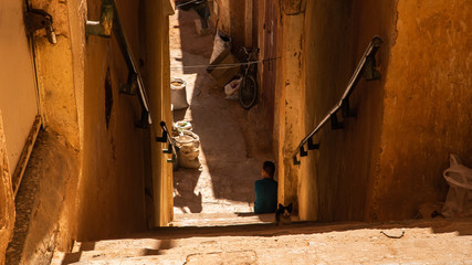 Boy sitting below a staircase in desert old town Ghardaia in Algeria