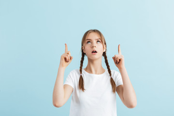 Young attractive girl with two braids in white t-shirt thoughtfully showing two fingers up gesture over blue background isolated