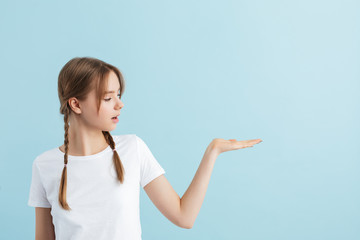 Young pretty girl with two braids in white t-shirt dreamily looking aside showing invisible copyspace over blue background isolated