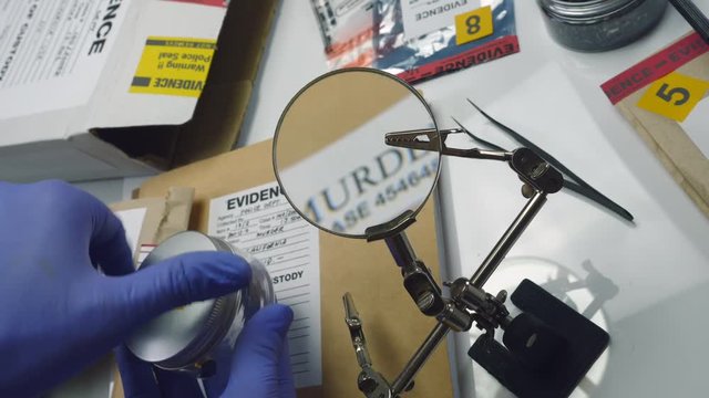Police expert examines bullet cap with magnifying glass in scientific laboratory