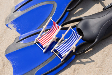 concept of summer and relaxation, a pair of flippers lies on the sand, two small lounge chairs stand on flippers