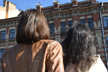 young ladies tourists in Saint Petersburg Russia stand on a bridge at a yellow buildings square and watch architectural details of a building