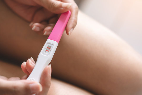 Young asian woman holding pregnancy test showing a positive result in bedroom, Wellness and healthy concept, Abortion problem, Selective focus.