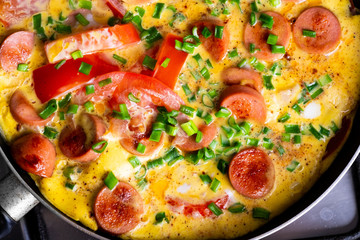 Omelette with tomato, onion and sausage on frying pan