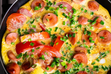 Omelette with tomato, onion and sausage on frying pan