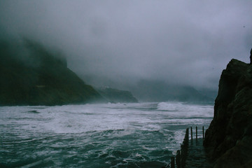 Fototapeta na wymiar Waves of a raging dark sea crashing on rocks