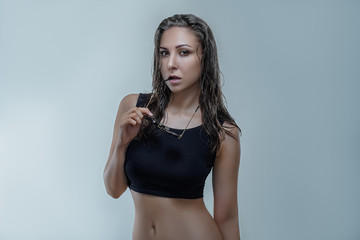 Fototapeta premium Beautiful woman in black shirt with wet hair is posing stylishly with round black sunglasses isolated on gray background in a studio. Fashion accessories photography with slim and sexy female model