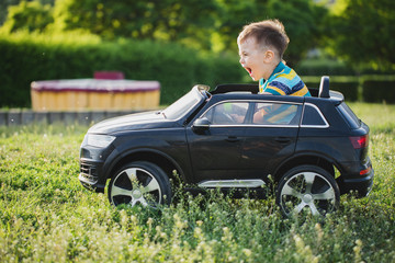 Cute boy   riding on black electric car in the park. Funny boy rides on a toy electric car