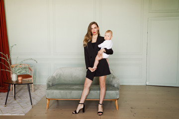 young beautiful blonde girl in stylish classic clothes in black with a baby in white apartment