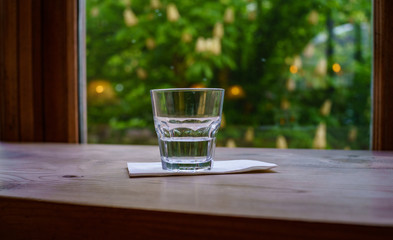 One glass of water on a white napkin on a wooden table near a window overlooking the avenue with blooming chestnut trees. Art photography