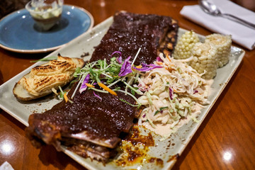 A plate of delicious and juicy pork rib with baked potatoes, salad, and corns.