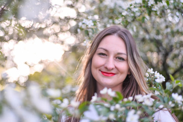 Woman with long blond hair in the garden with flowers. Beautiful girl on a sunny day.