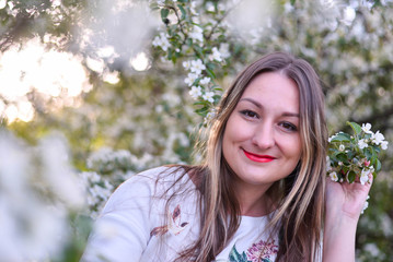 Woman with long blond hair in the garden with flowers. Beautiful girl on a sunny day.