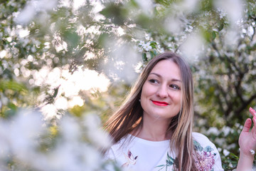 Woman with long blond hair in the garden with flowers. Beautiful girl on a sunny day.