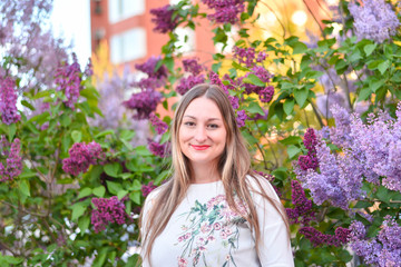Woman with long blond hair in the garden with flowers. Beautiful girl on a sunny day.