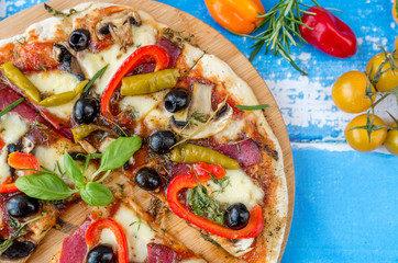 Widok z góy na pyszną pizzę z wieloma składnikami. Obok pomidory i zioła. © Michał
