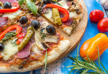 Pizza domowa z różnymi składnikami. Obok pomidory i gałązka rozmarynu. © Michał