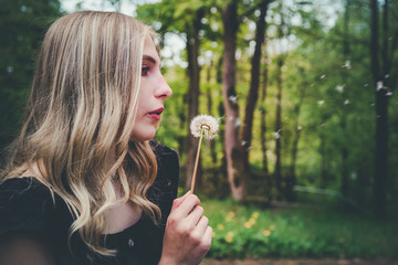 Attractive blond woman blowing on a dandelion