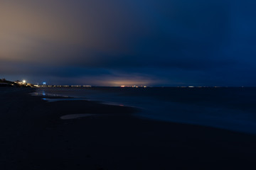 Mysterious lights of a distant port seen from a beach at night.