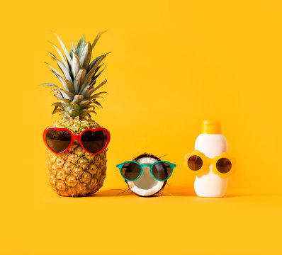 Pineapple and coconut wearing sunglasses with sunblock on a solid background