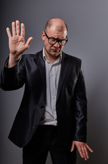 Obraz premium Unhappy depressed busuness man in black suit and glasses showing the palm stop sign on grey background. Closeup
