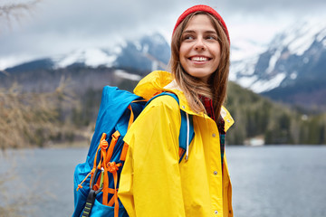 Horizontal view of optimistic European female tourist looks happily aside, enjoys walking near...