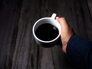 cup of black coffee in hand and wood ground