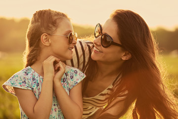 Happy fashion kid girl embracing her mother in trendy sunglasses and looking each other with love...