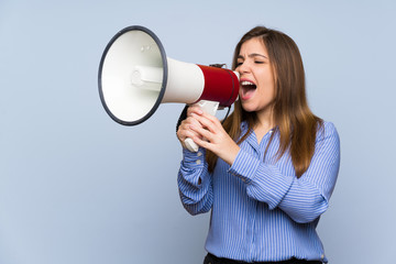 Young girl over isolated blue wall shouting through a megaphone