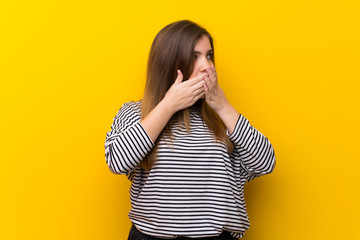 Young girl over yellow wall covering mouth and looking to the side