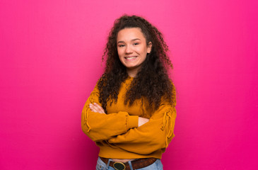 Teenager girl over pink wall with arms crossed and looking forward