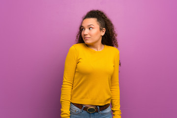 Teenager girl over purple wall making doubts gesture looking side