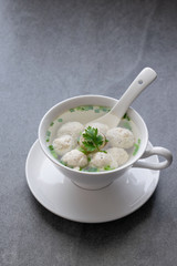 Chicken ball soup with scallion in white bowl on table.