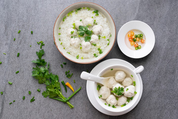 Rice soup with chicken ball and scallion in gray bowl on table.